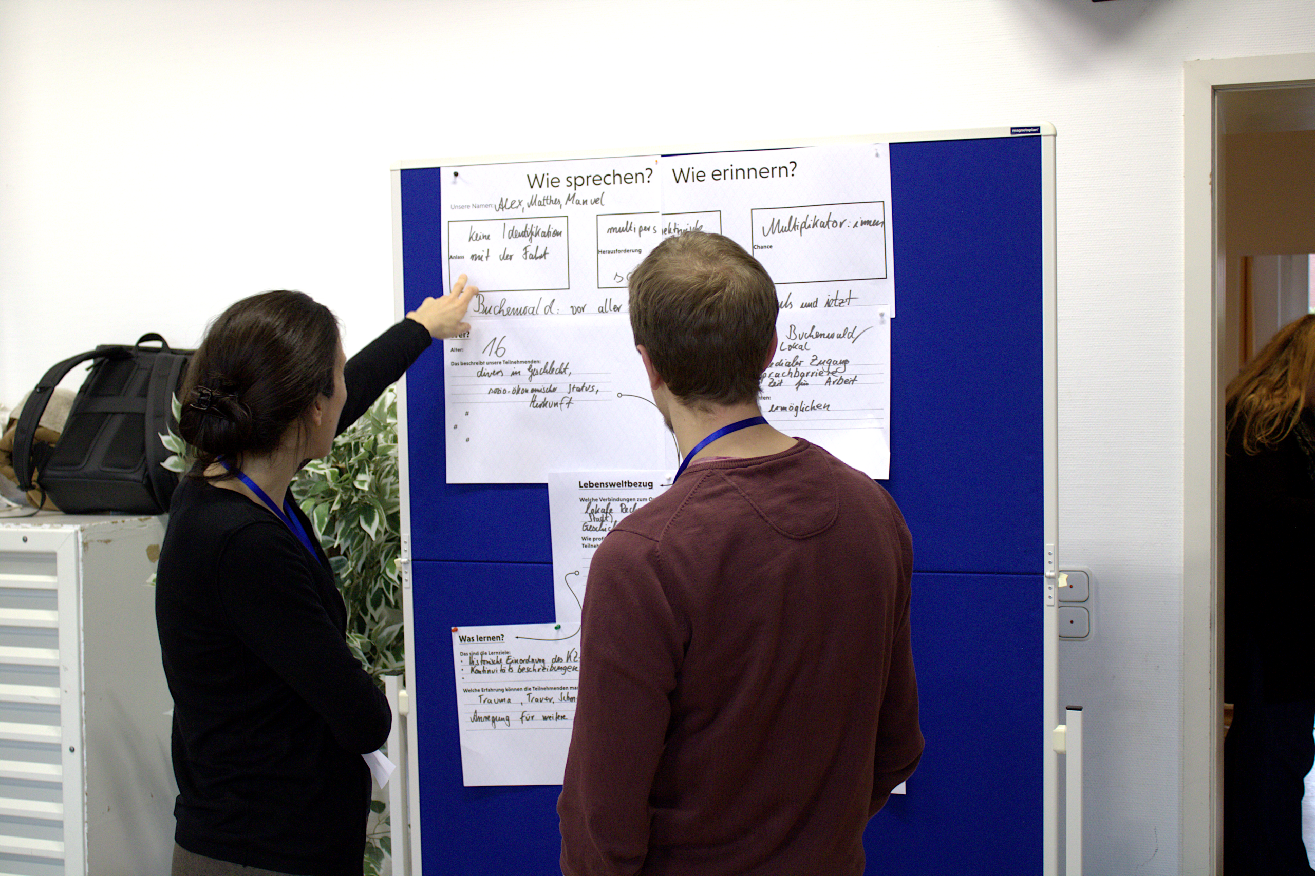 Zwei Teilnehmende stehen an der Pinnwand und betrachten ein Ergebnis aus dem Workshop: Eine Gedenkstättenfahrt nach Buchenwald